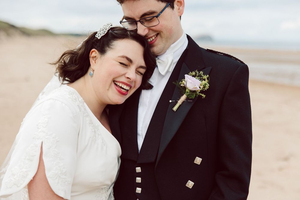 Newlywed couple sharing romantic moments on a sandy beach in formal wedding attire.