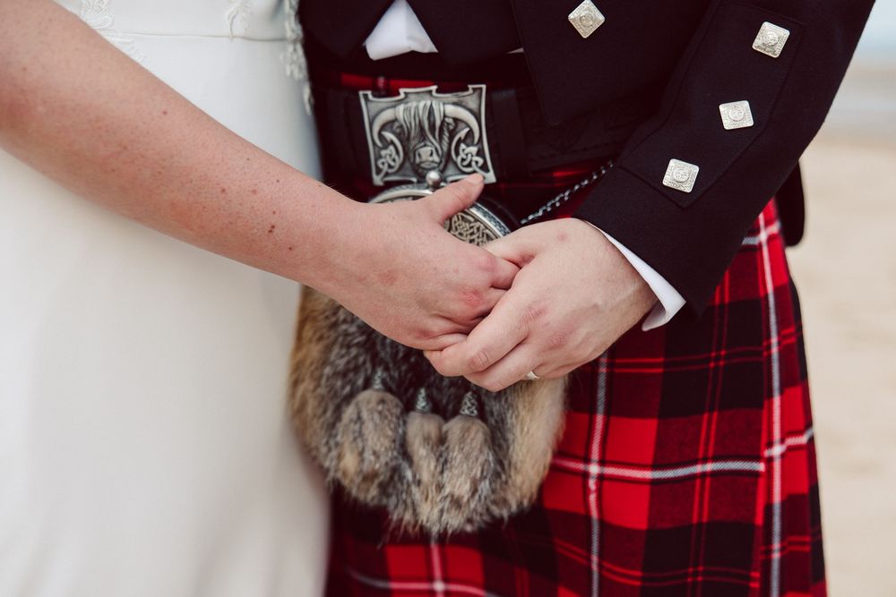 Close up detail of hands against traditional red tartan kilt with sporran and decorative silver accents.