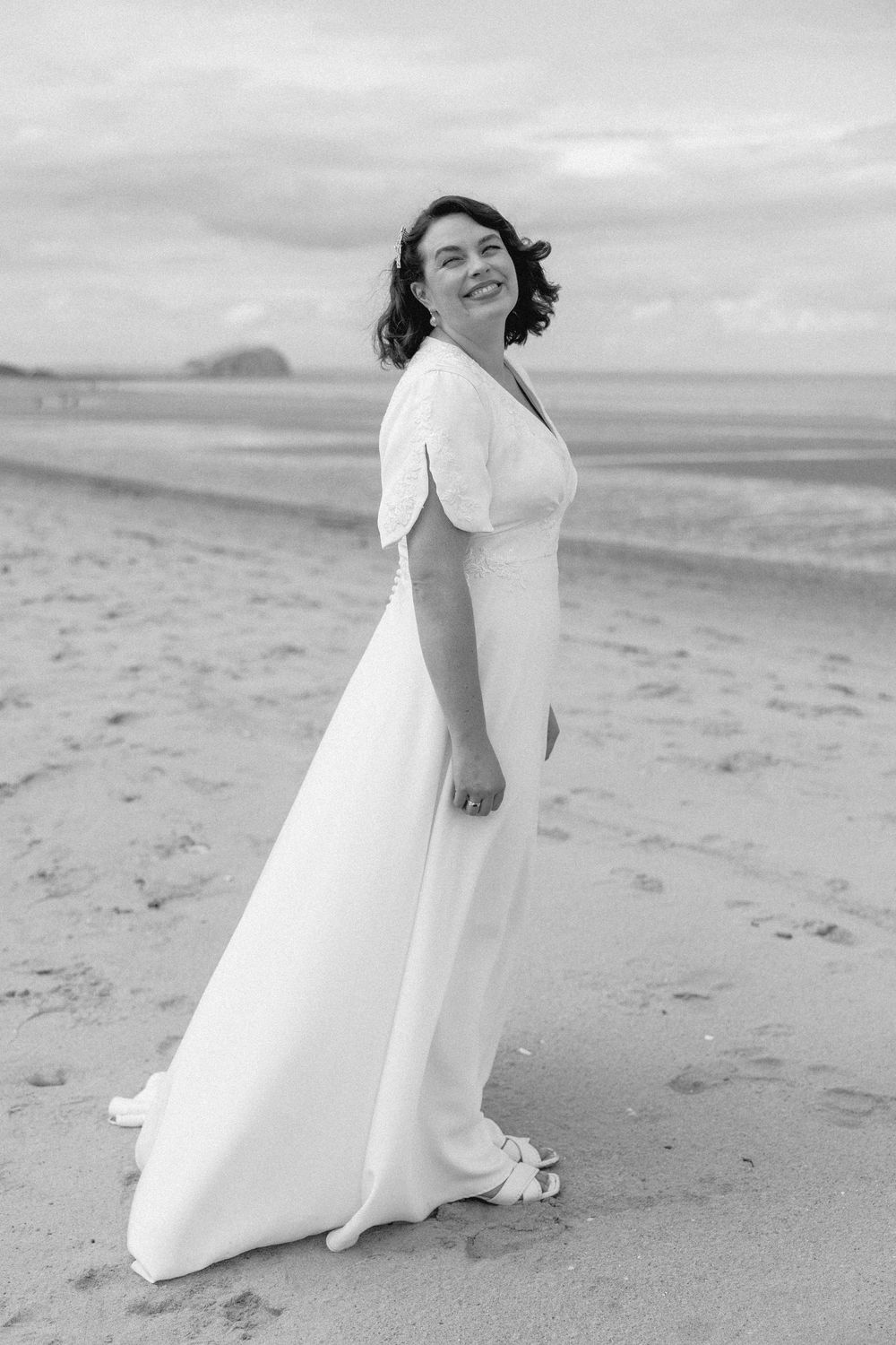 A joyful figure in a flowing white dress twirls and dances on a misty beach with waves and mountains in the distance.