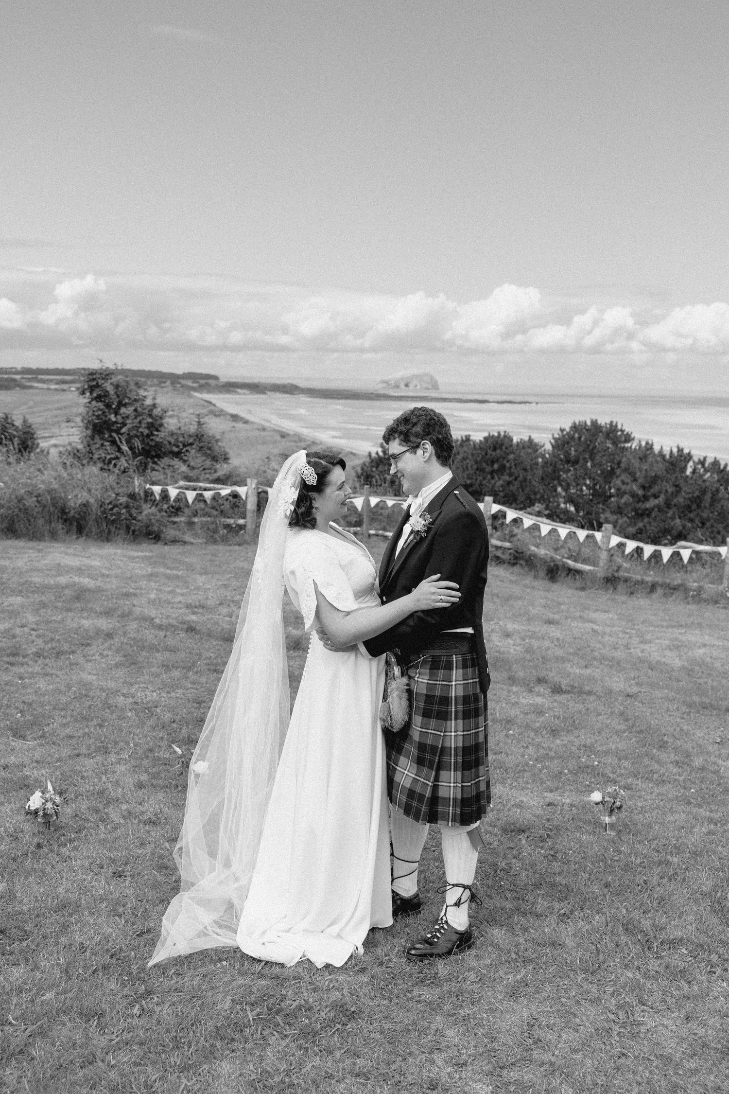 A romantic wedding couple embraces on a hilltop with decorative bunting flags in the background.