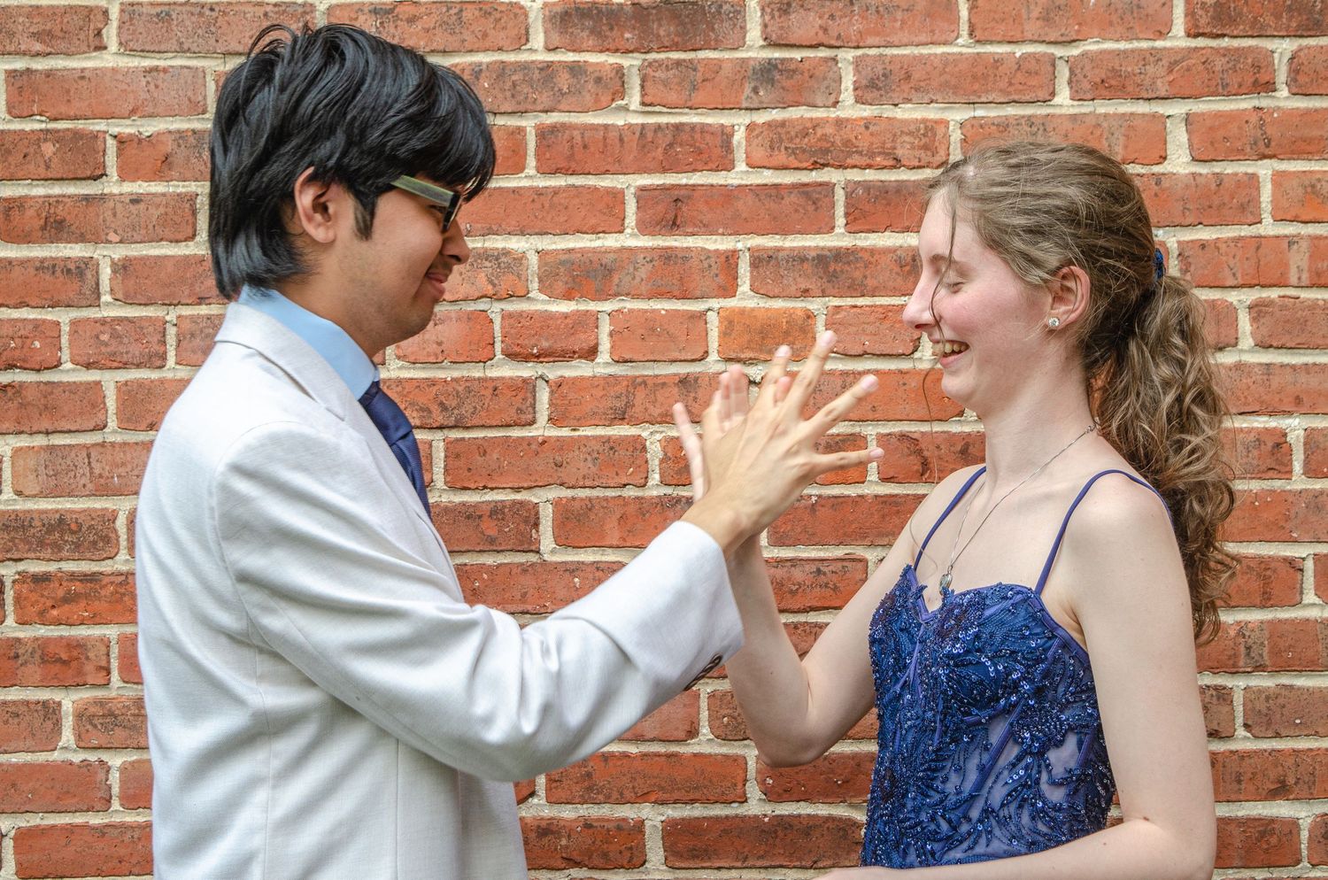 Two people engaged in expressive conversation while standing against red brick wall.