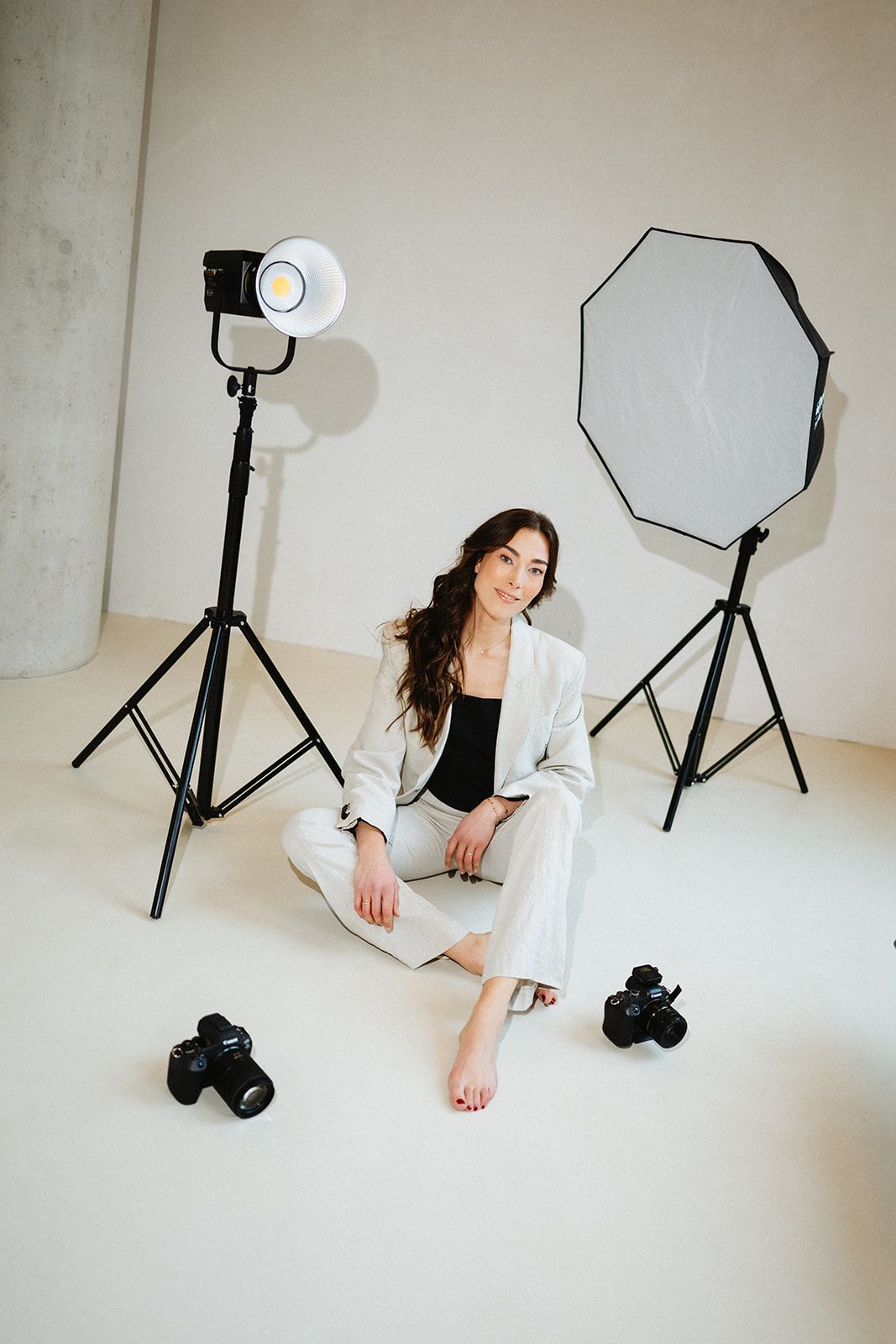 Photography studio scene with lighting equipment and person sitting on white floor.