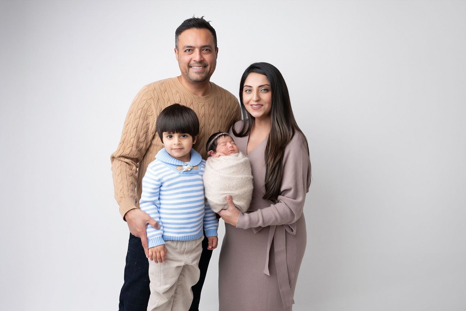 A family of four poses together against a white background wearing casual attire.