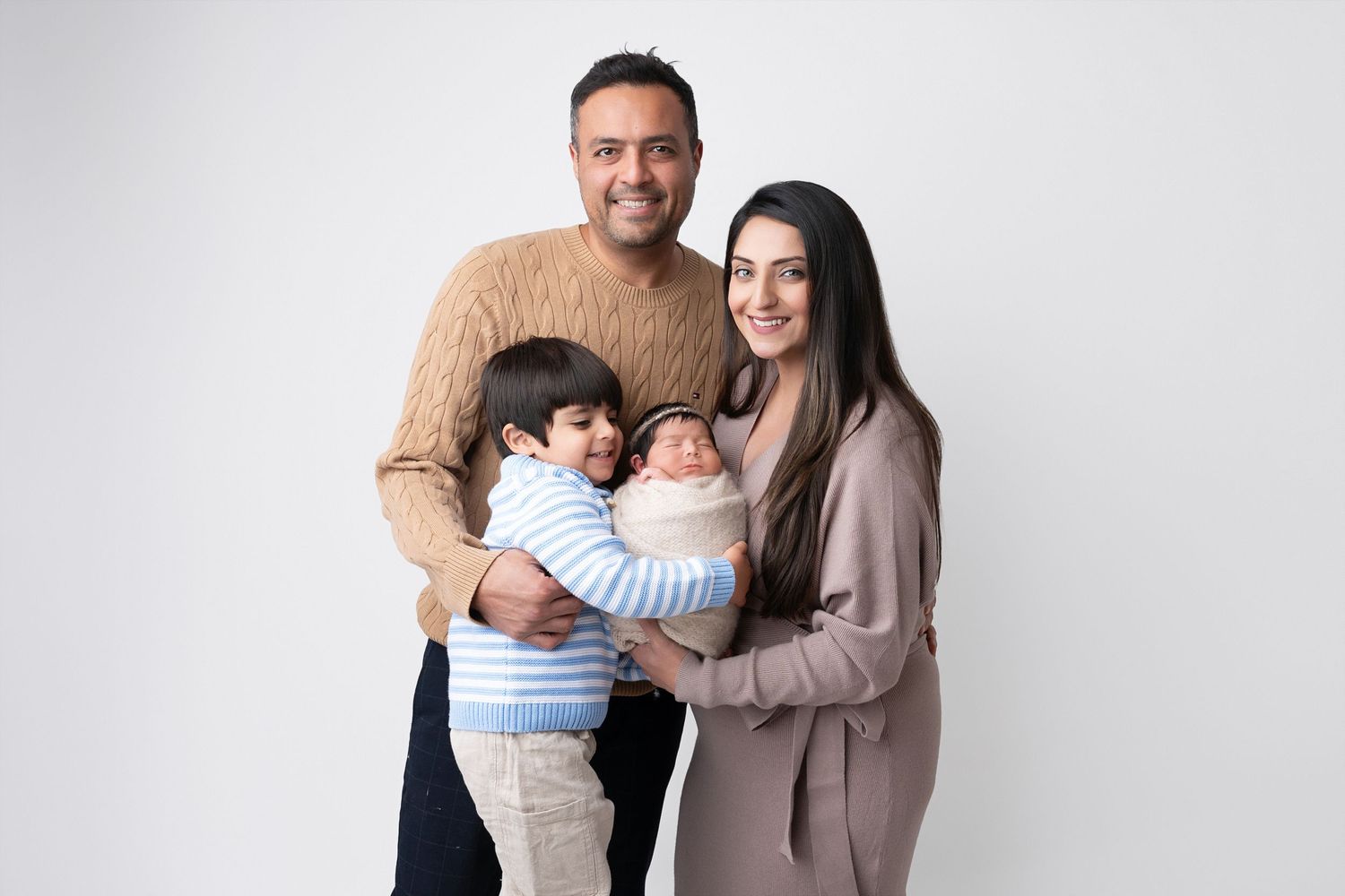 A family poses together in coordinated neutral outfits against a white studio background.