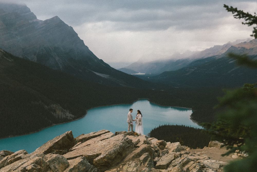 bride and groom hold hands on a rocky outcrop above a turquoise lake during their Banff Elopement
