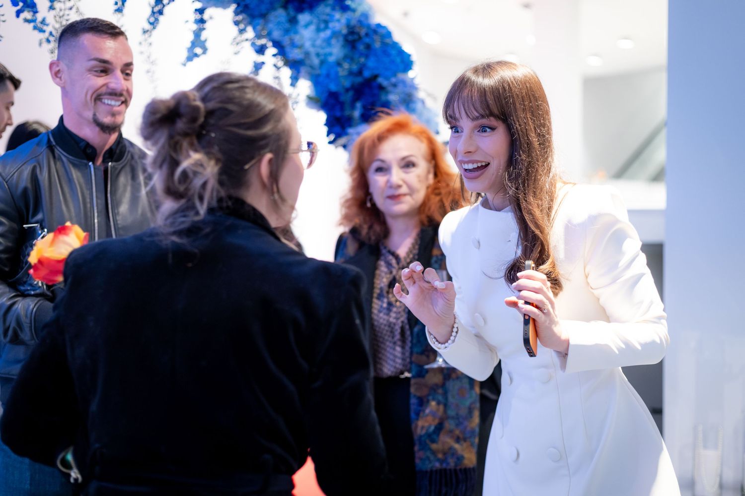 Guests socializing at upscale event with blue floral decor in background.