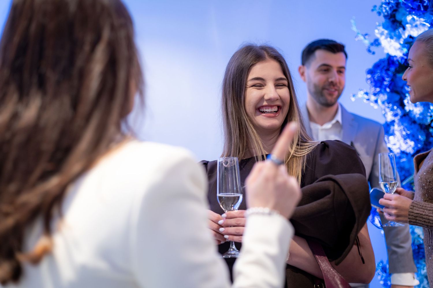 Young woman laughing holding champagne glass at elegant social gathering.