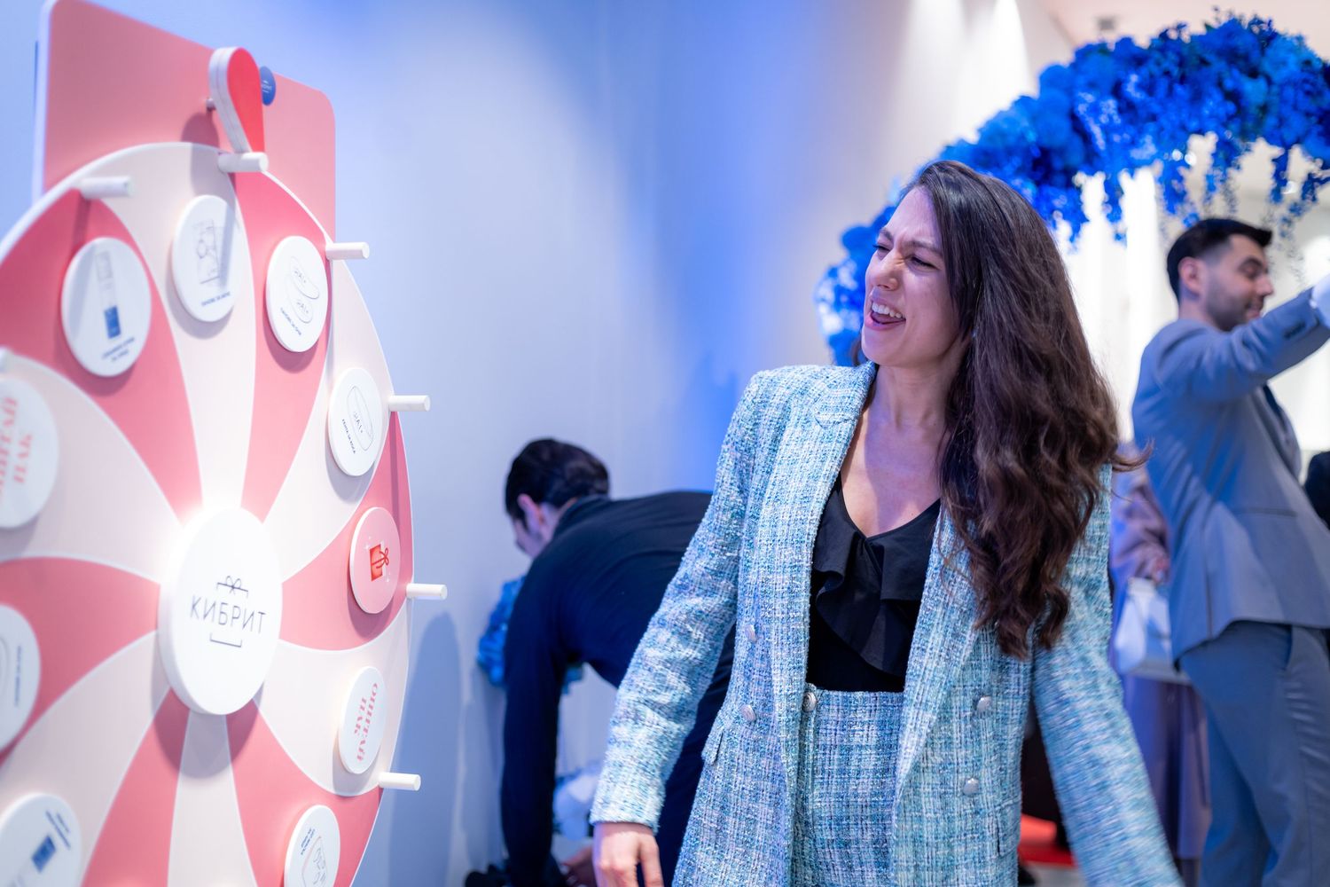Woman laughing beside prize wheel at branded cosmetics promotional event.