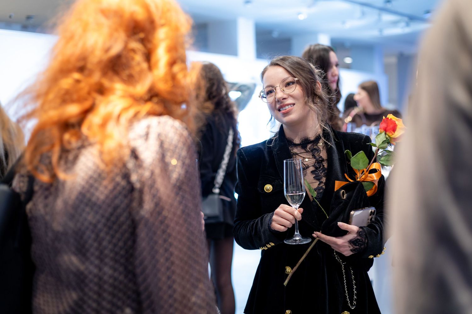 Woman smiling holding champagne and flowers at stylish social gathering.