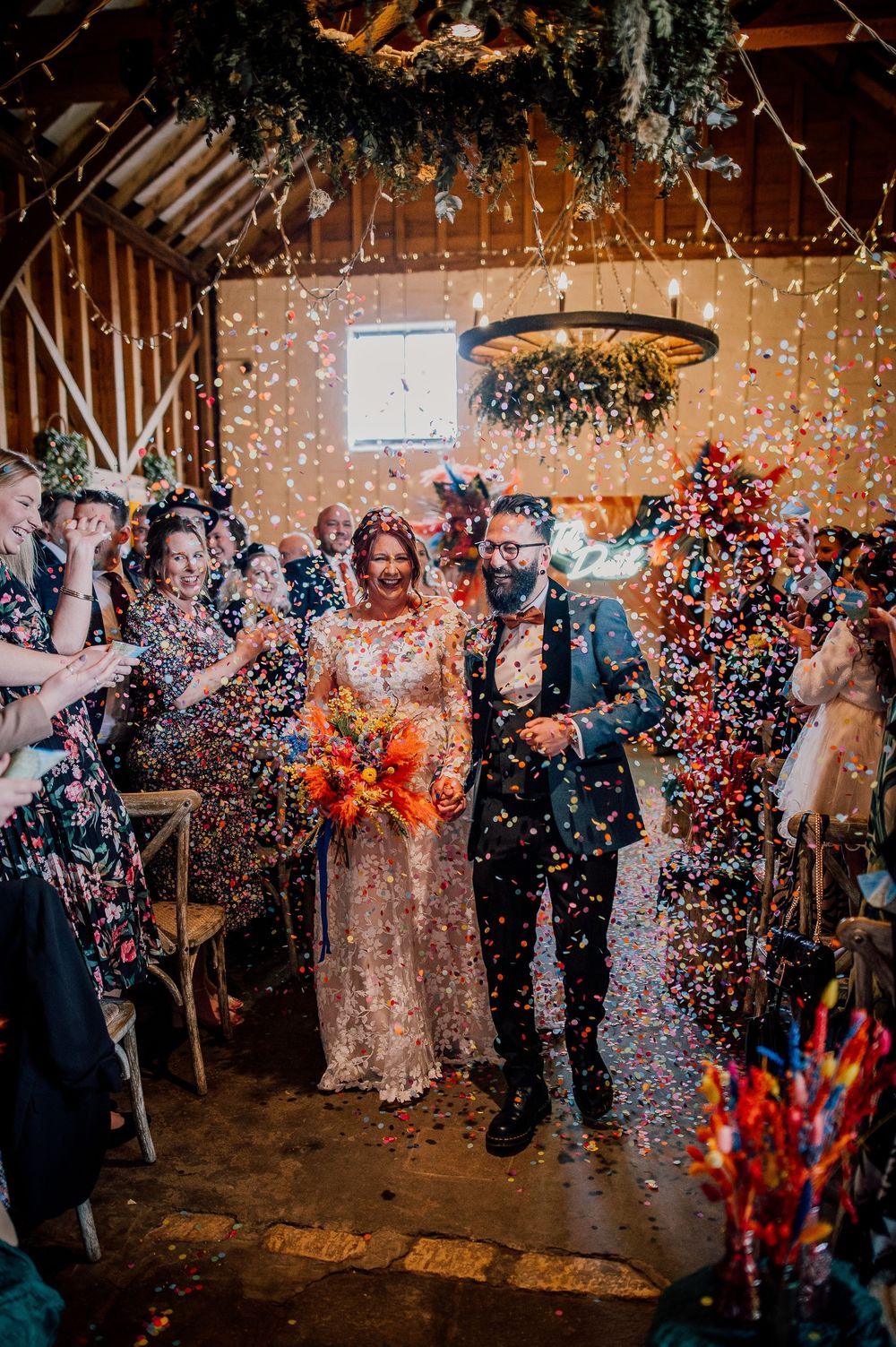 Festive wedding celebration with confetti falling in a rustic barn venue decorated with twinkling lights and greenery. Worcestershire Weddin