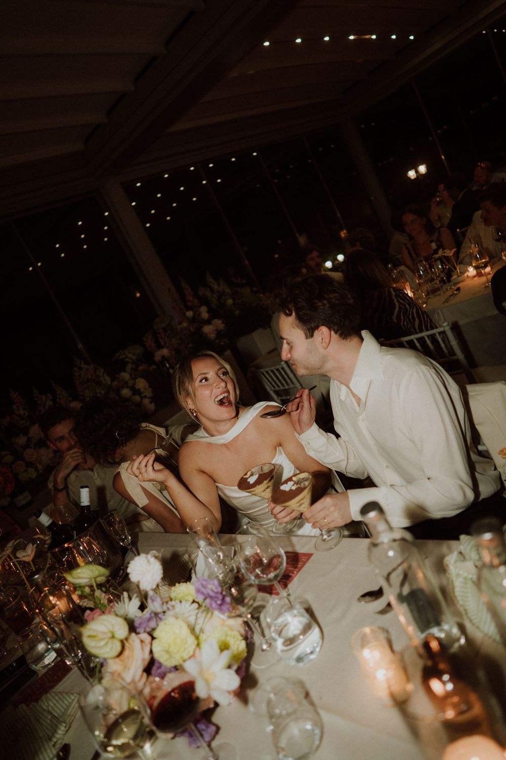 Candid moment at a wedding reception dinner table with guests laughing and interacting in warm candlelight at bourne and hollingsworth