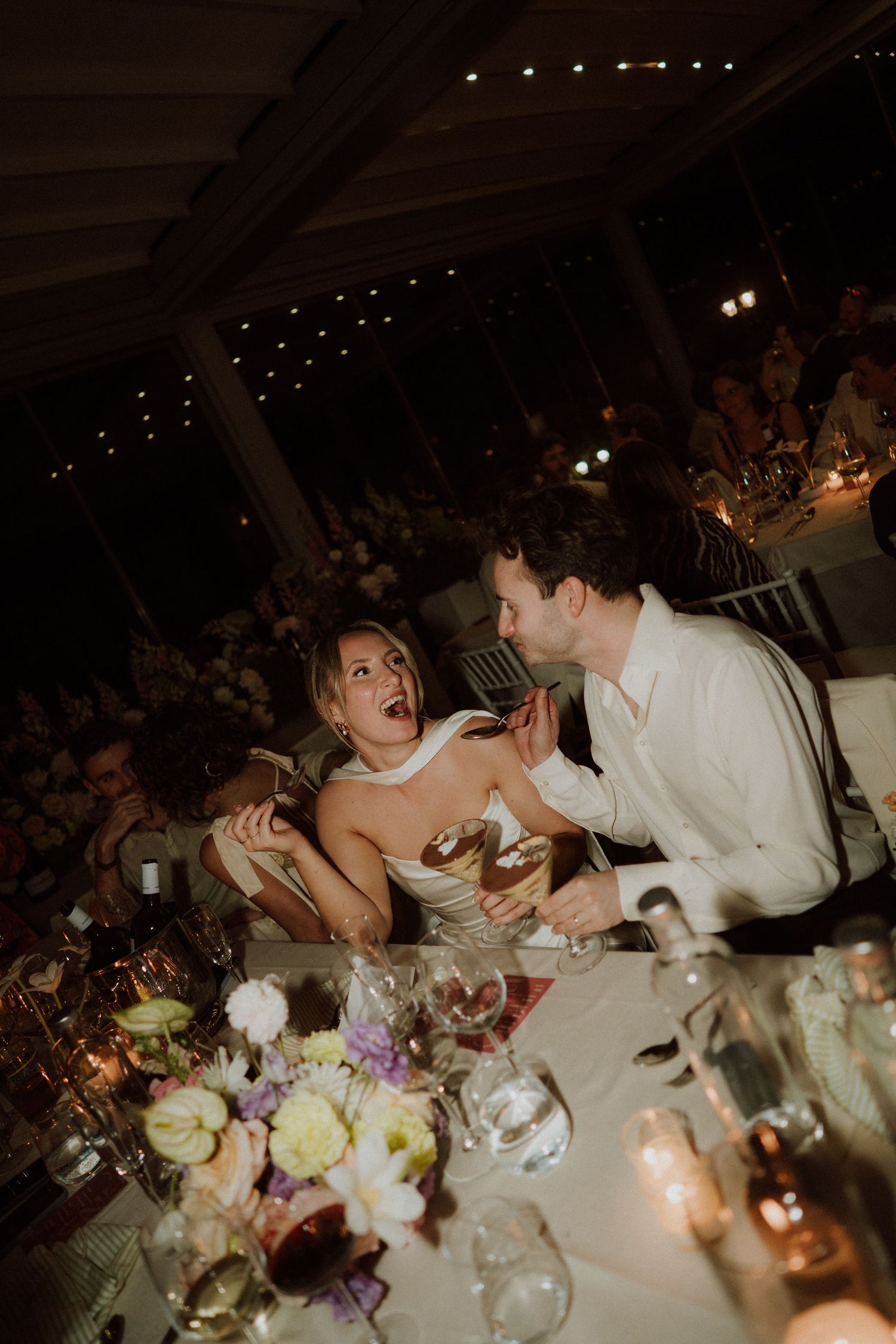 Candid moment at a wedding reception dinner table with guests laughing and interacting in warm candlelight at bourne and hollingsworth