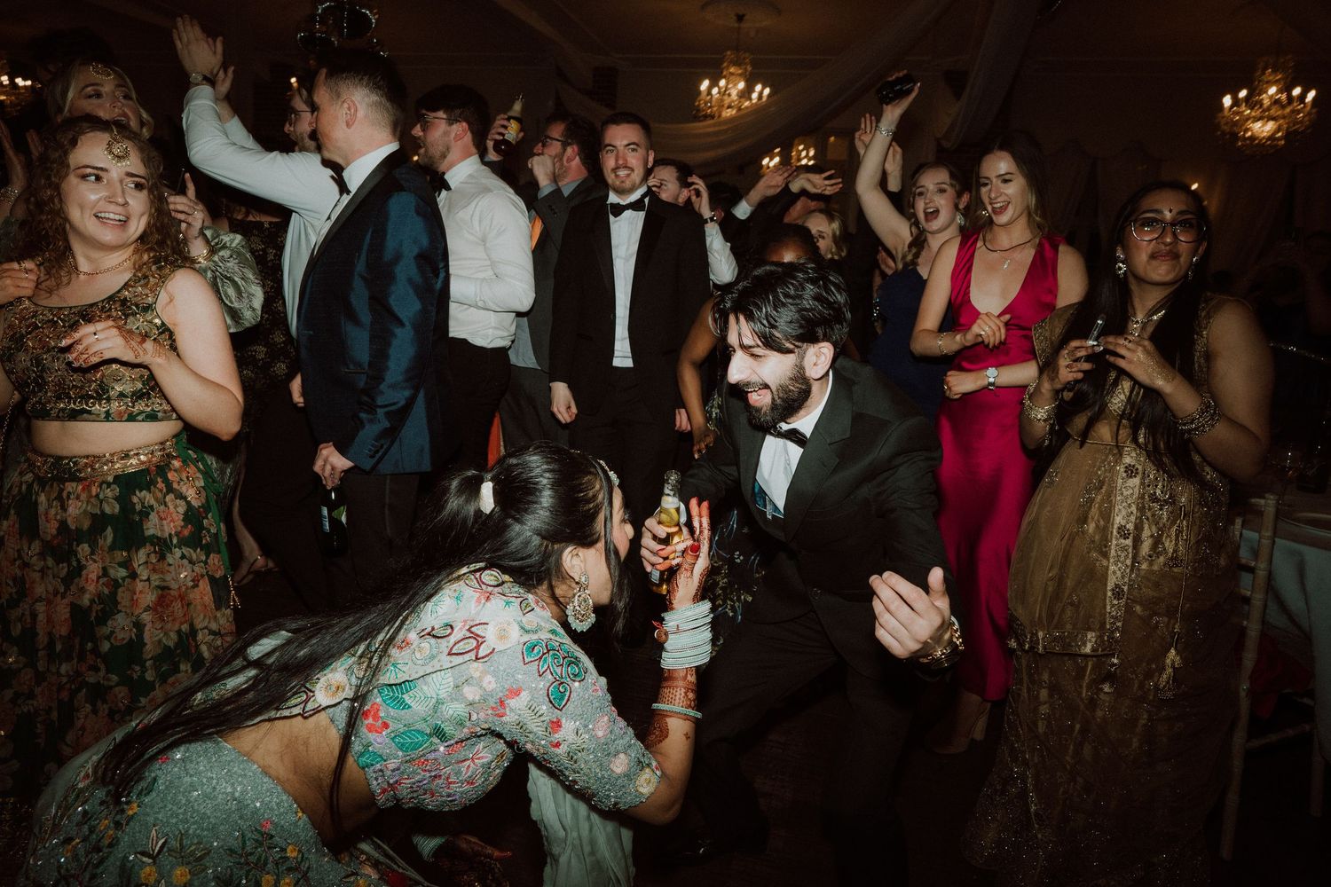 Wedding guests dance and celebrate together on a dimly lit dance floor during an evening reception.