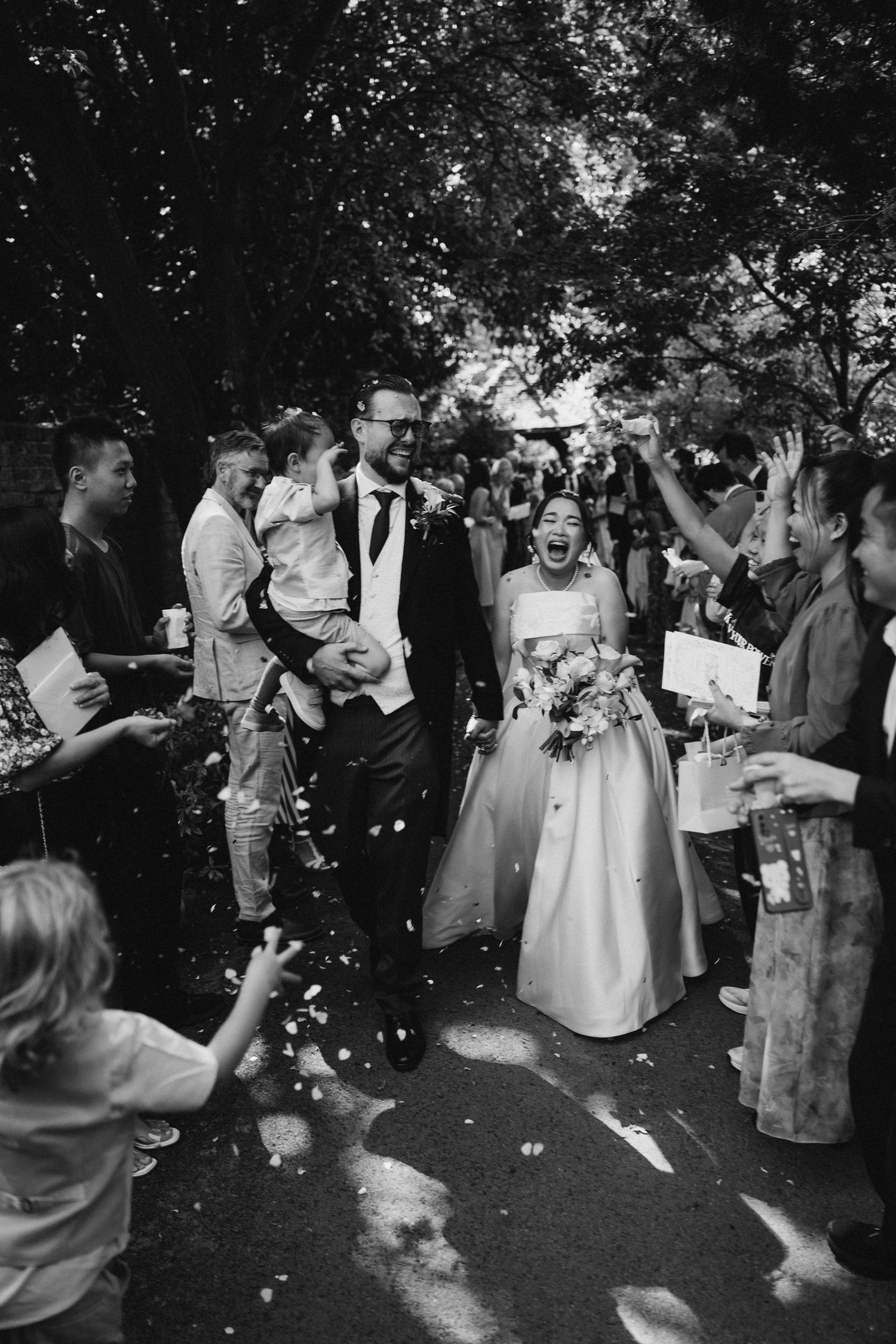 Wedding guests celebrate and dance during an outdoor reception as flower petals fall through the air at a Cotswold church wedding