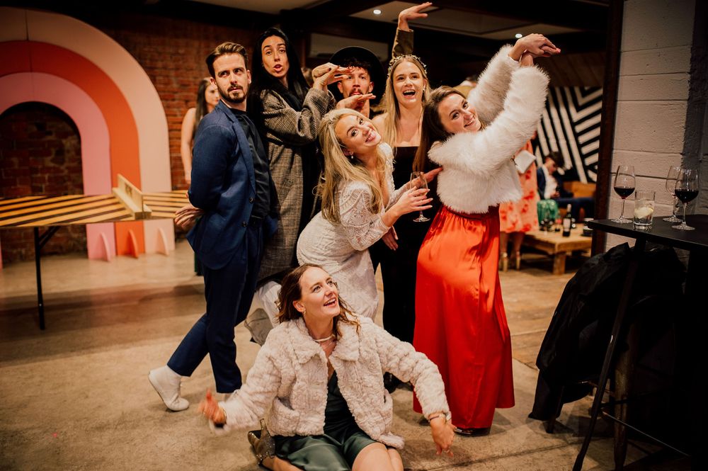 Wedding guests dancing and celebrating joyfully on a dance floor at an indoor reception venue.