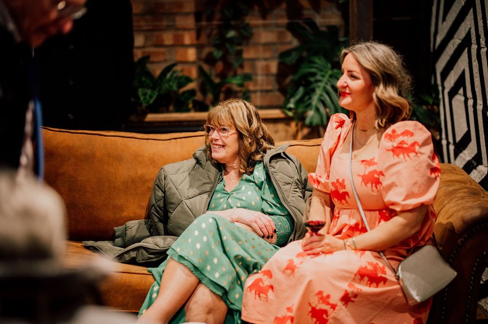 Two women in colorful dresses share a joyful moment while sitting together on outdoor steps.