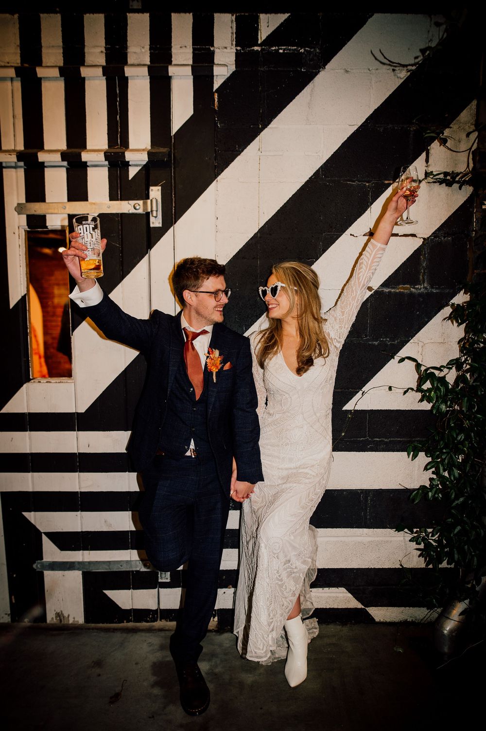A couple in wedding attire poses playfully against a black and white striped wall in a series of candid shots.