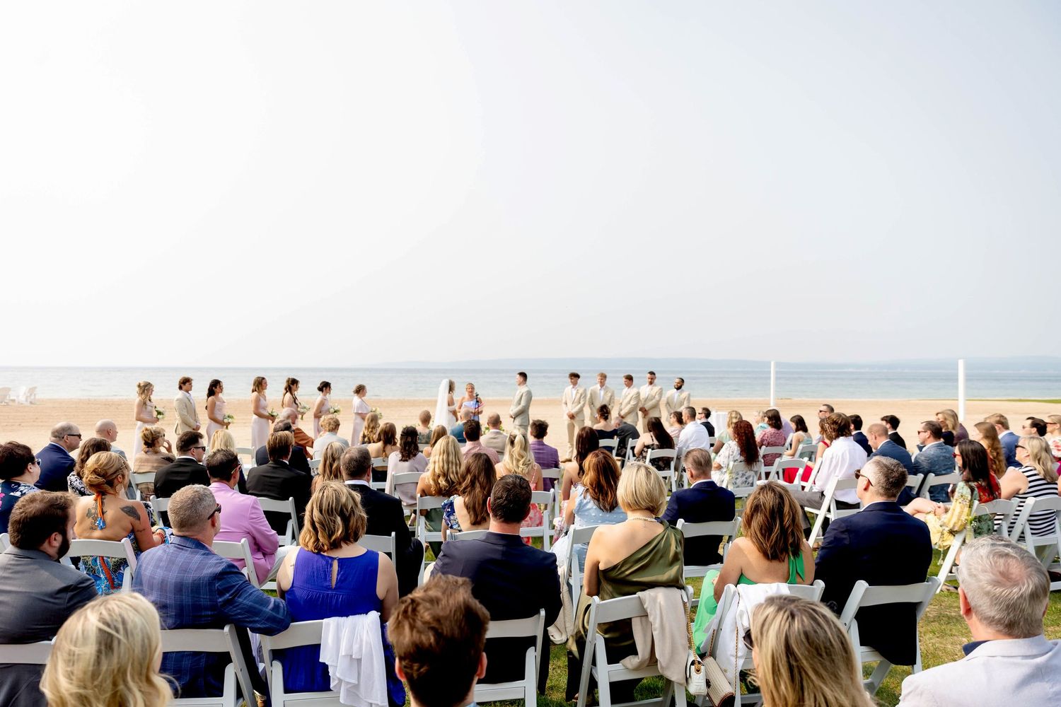Guests seated outdoors at a beachside ceremony during a June wedding at Sunset beach at Bay Harbor in Petoskey Michigan.