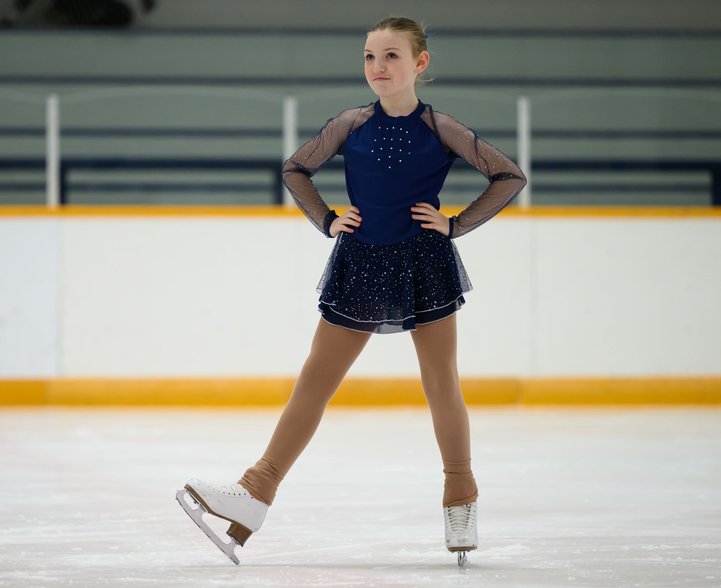 A figure skater in a navy blue dress performs a graceful spin sequence on the ice rink.