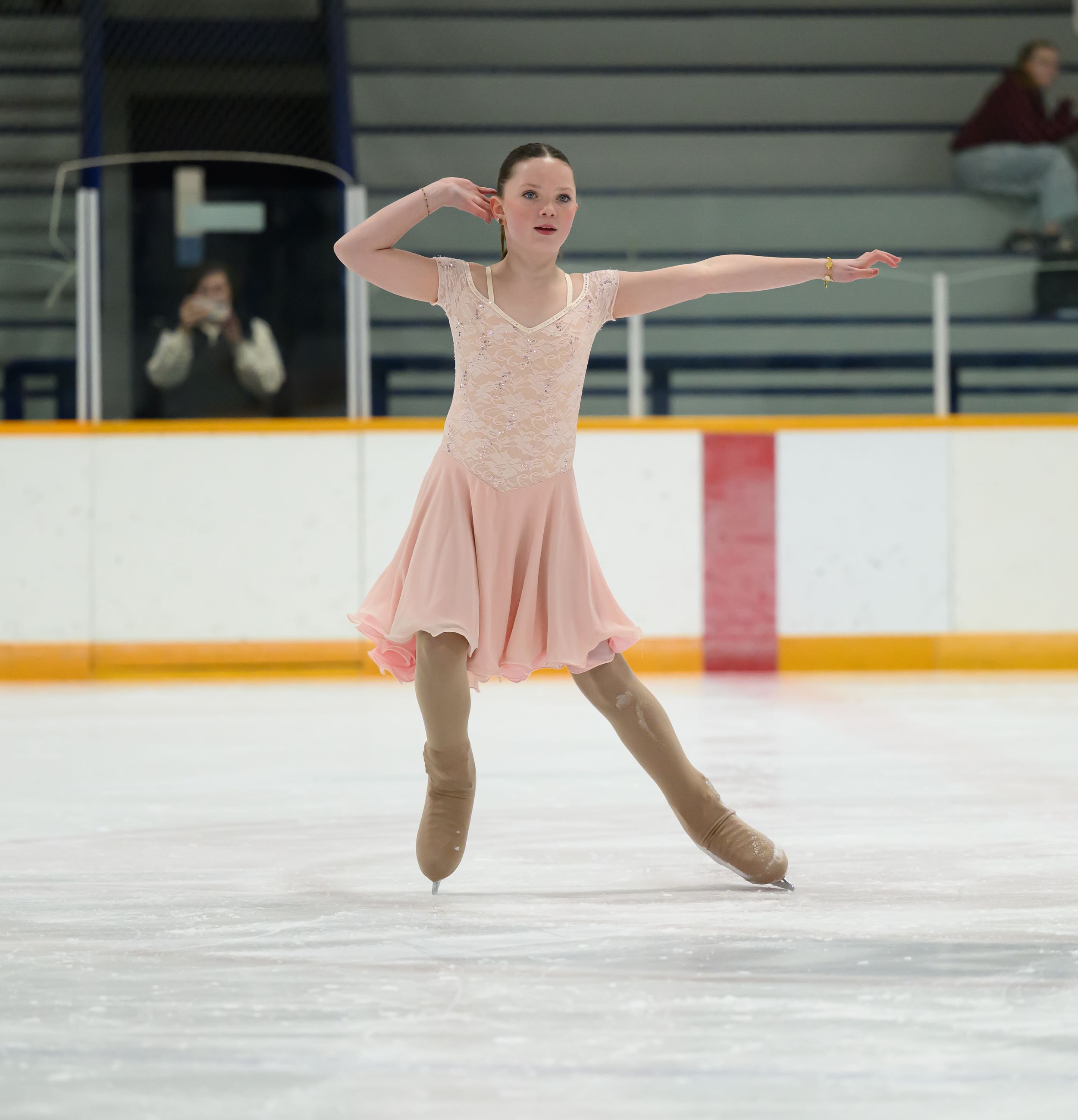 Figure skater in pink dress performs graceful spin on ice during competitive routine at indoor rink.