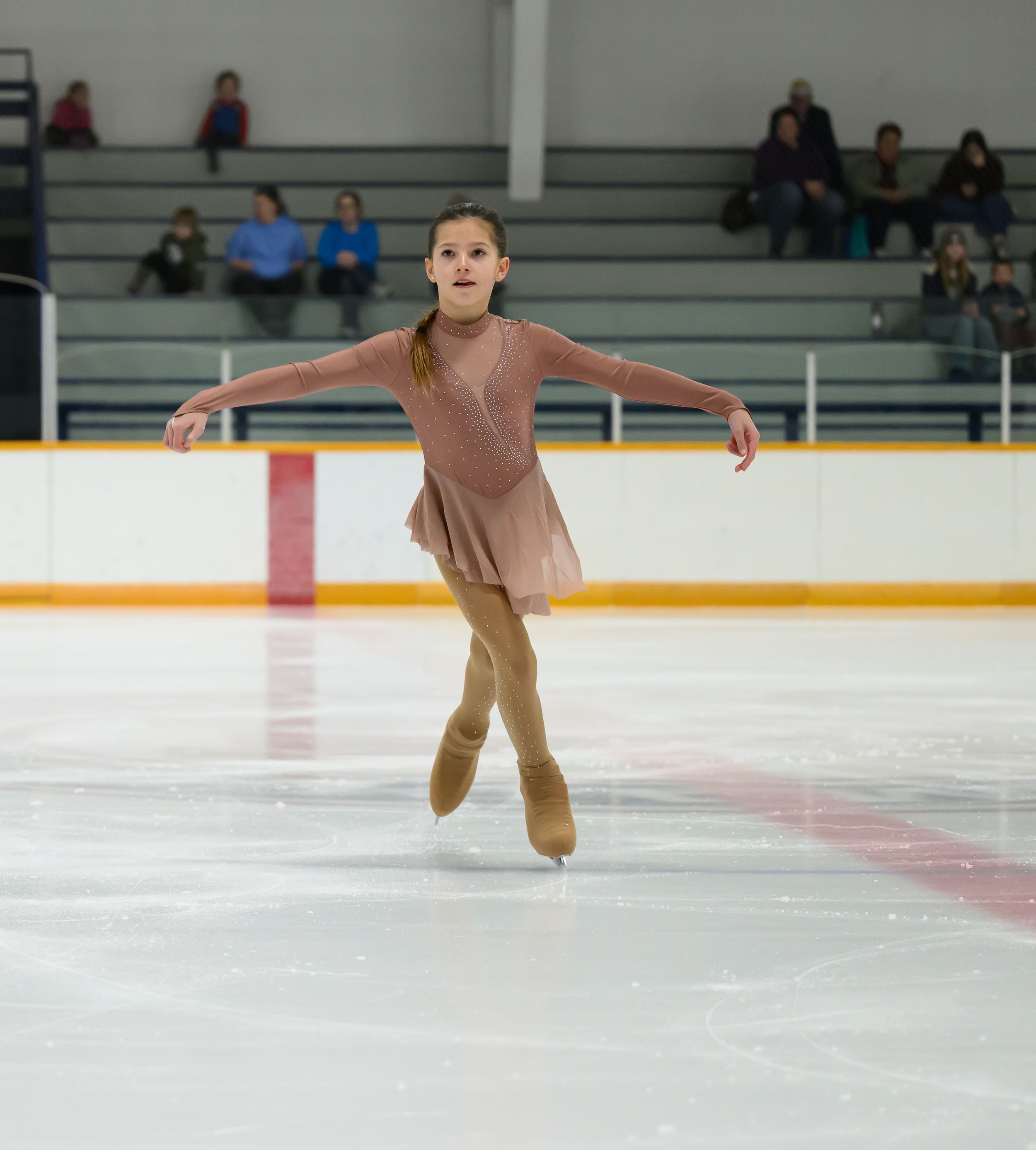 Figure skater performs graceful spin on ice during competitive routine at indoor arena.