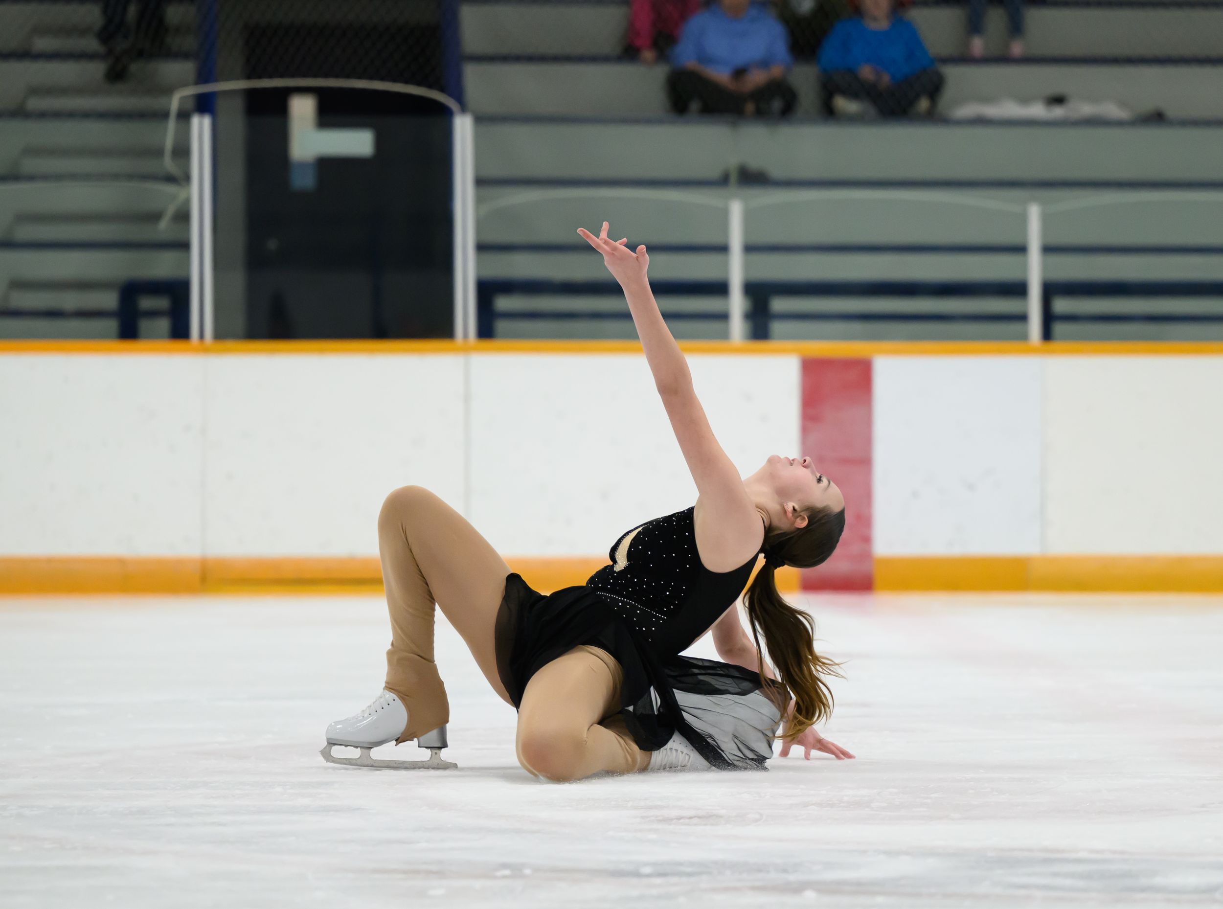 Figure skater in black dress performs graceful layback spin on ice during competitive routine.