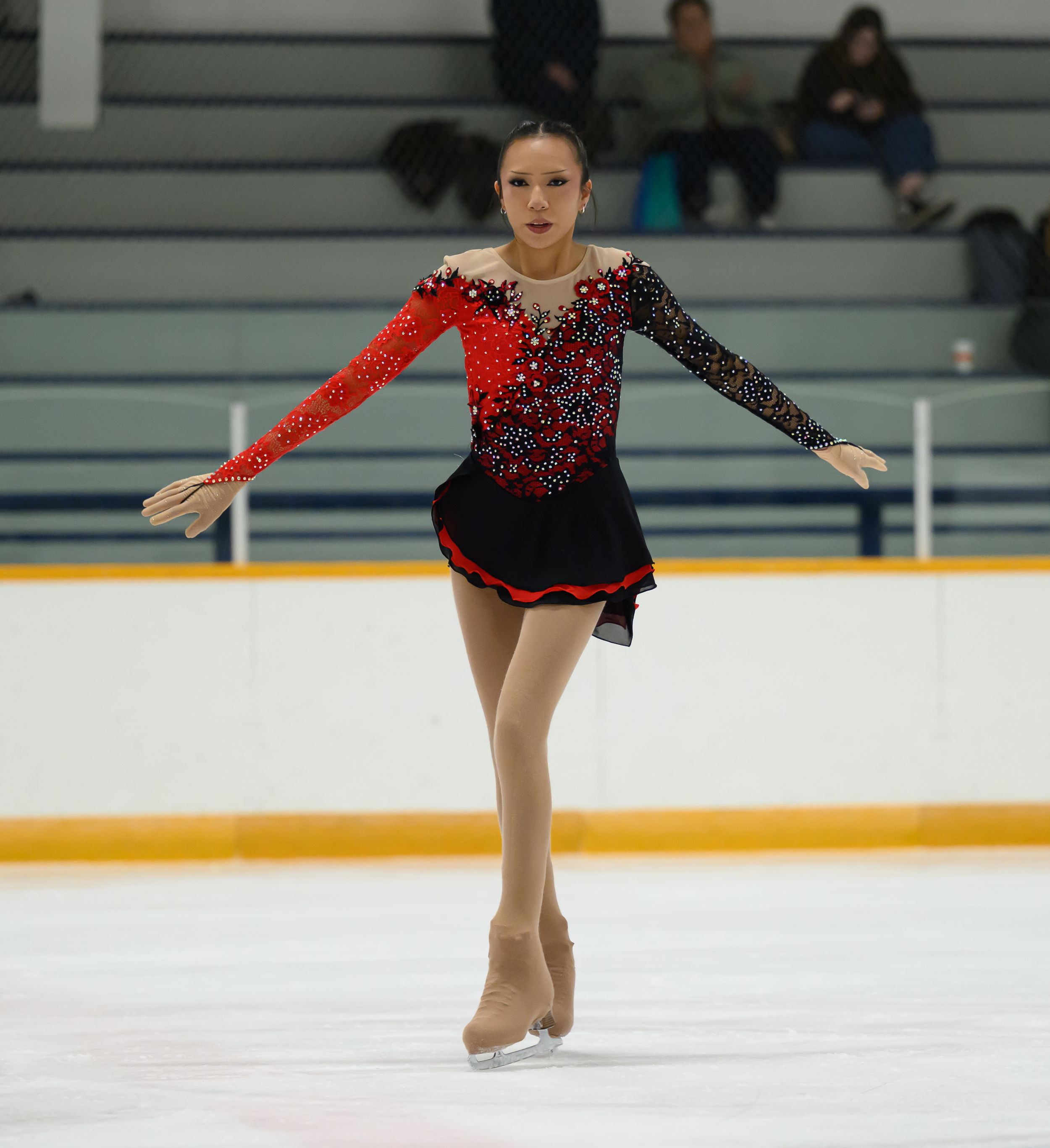 Figure skater in red and black costume performs graceful spin on ice during competitive routine.
