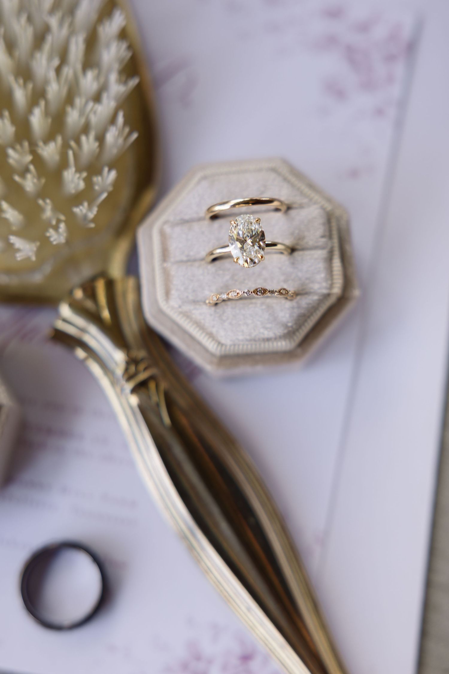 Elegant engagement ring with oval diamond in velvet ring box next to vintage gold hairbrush.
