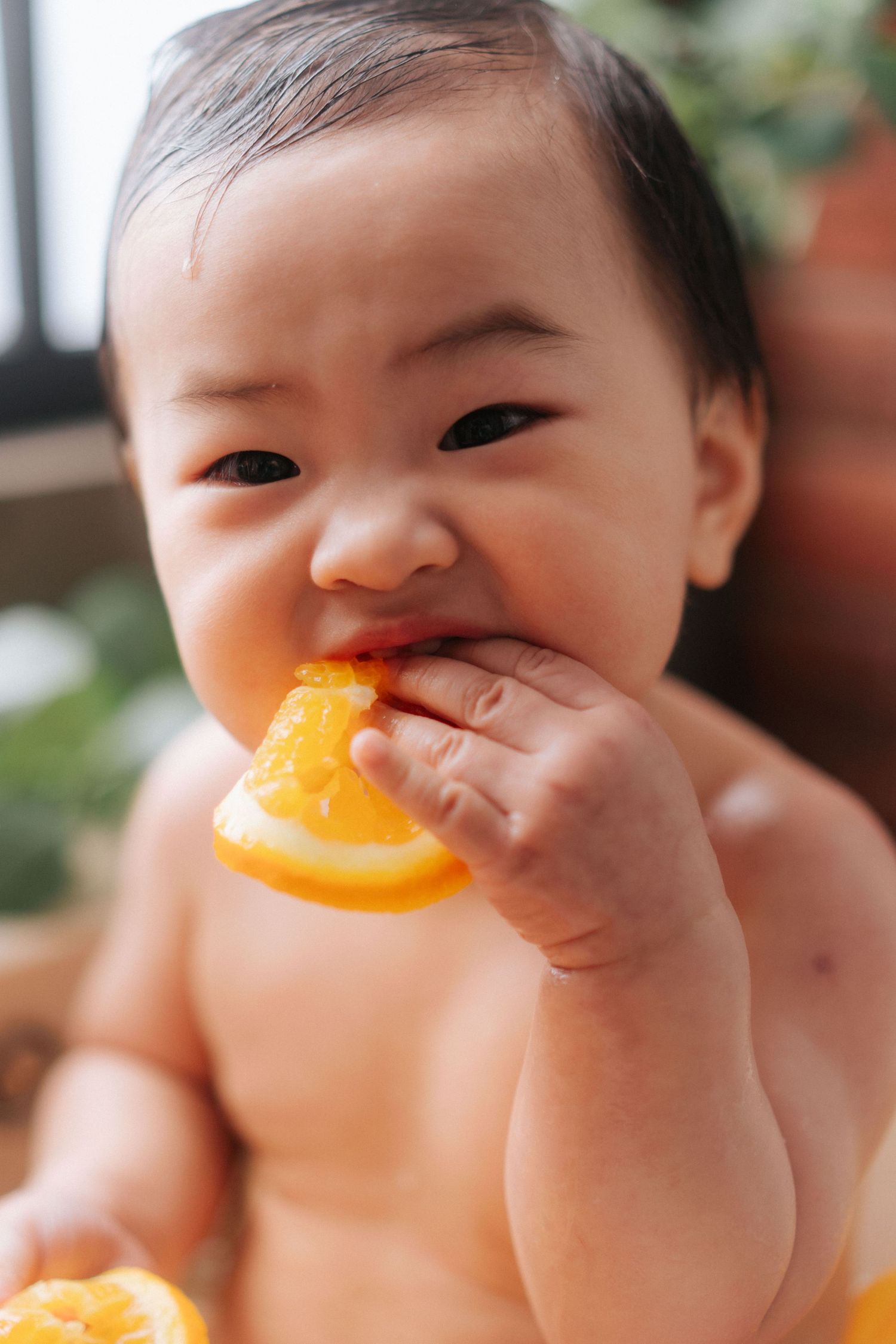 A baby sits in a highchair making expressive faces while eating during mealtime.