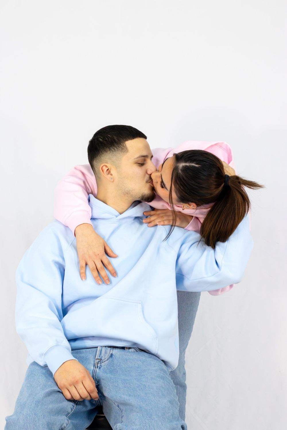 A couple in light blue sweaters and jeans share an intimate moment against a white background.