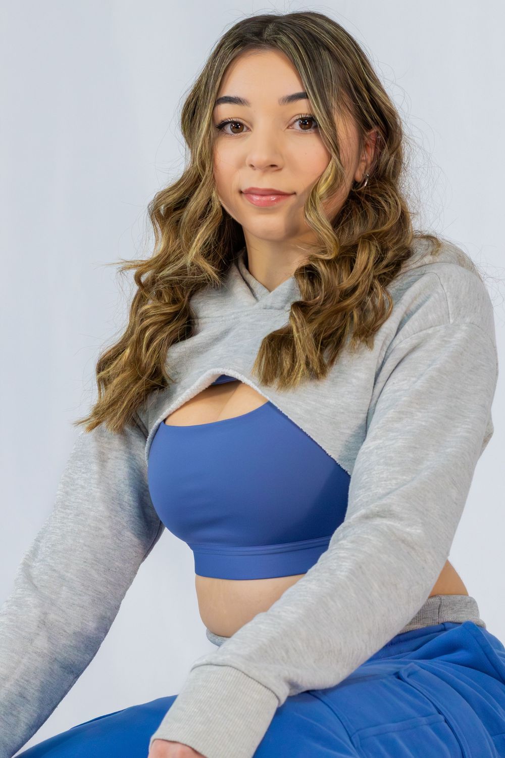 A person poses in a blue sports bra and grey cardigan showing different angles and expressions.