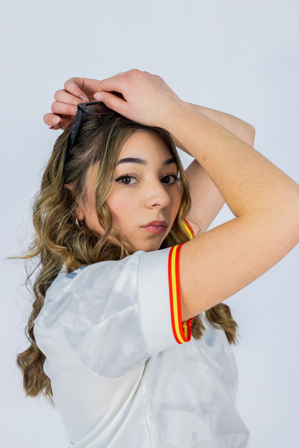 Person wearing white top with red and yellow striped cuffs poses playfully against light backdrop.