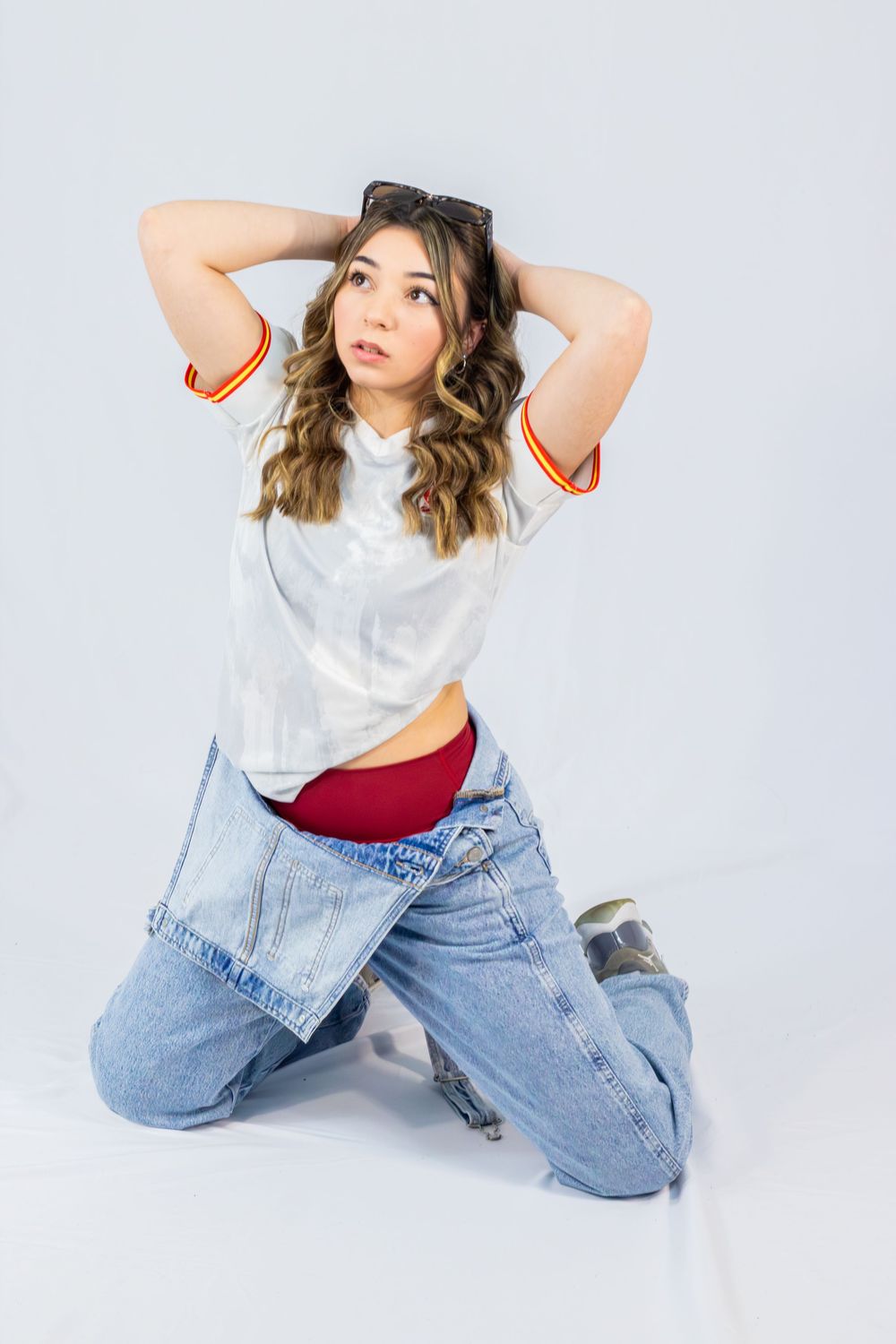 Fashion model in white t-shirt and baggy jeans poses on studio floor against light background in various positions.