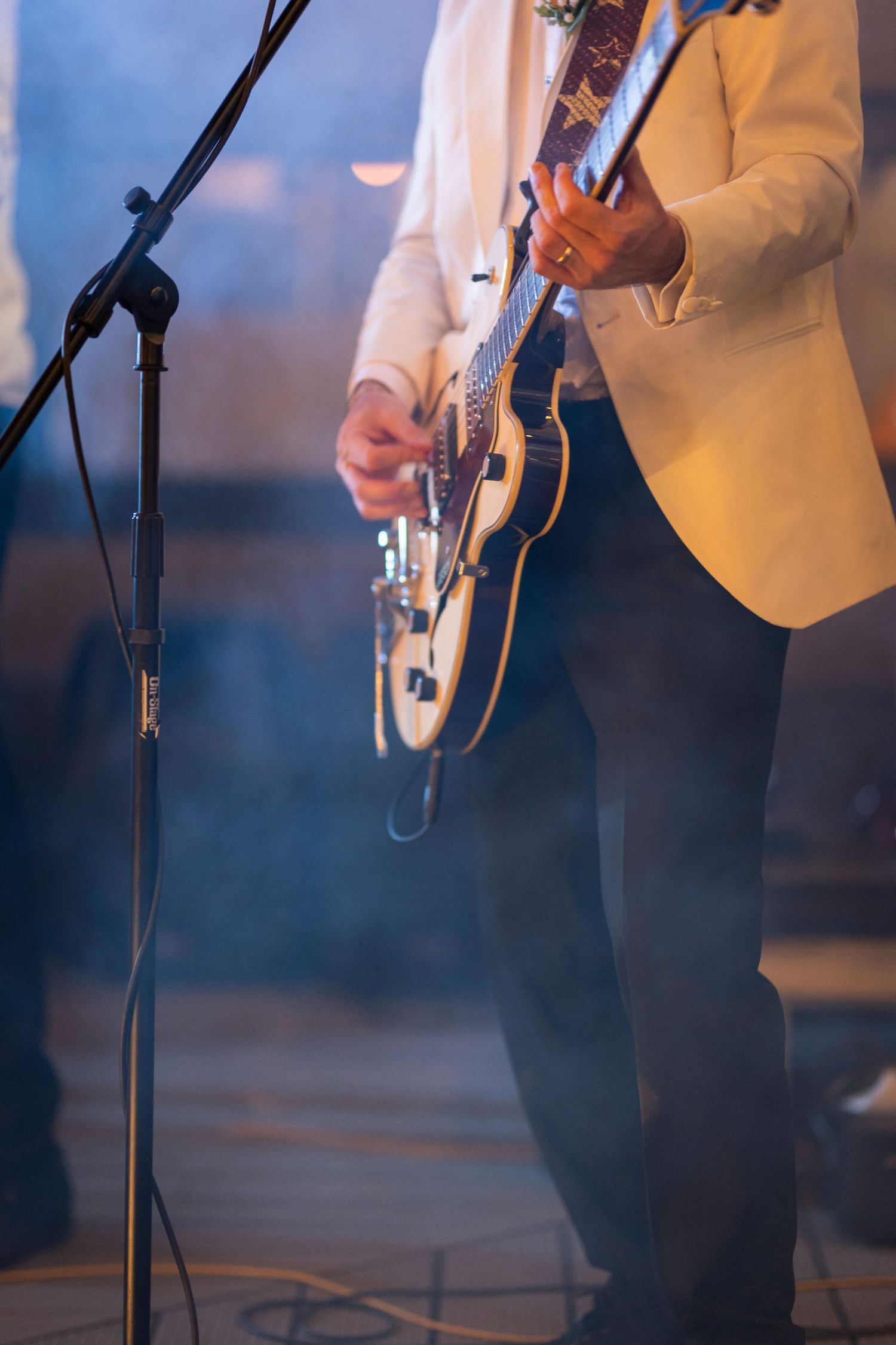 Musician in yellow blazer performs on stage with guitar and microphone stand during live performance.