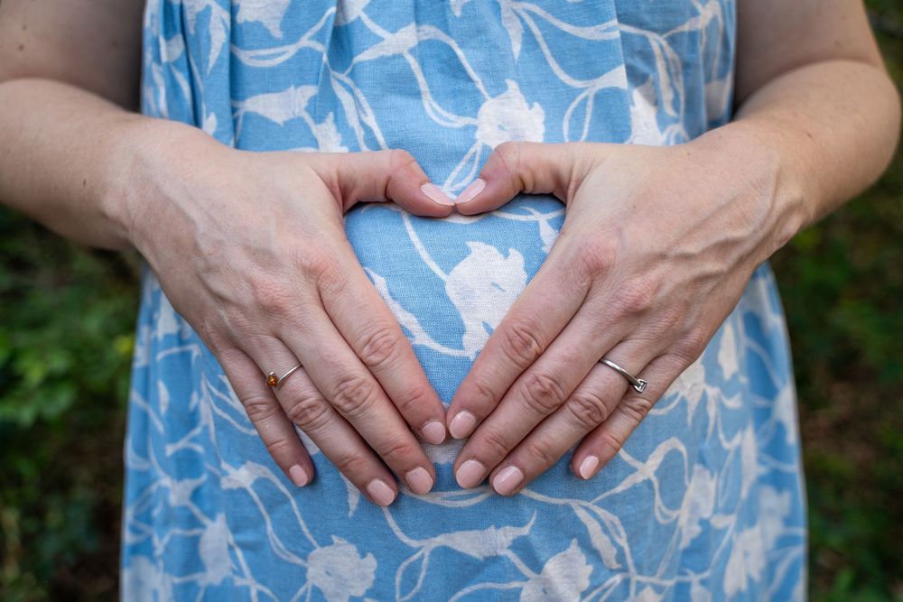 Close-up photos showing hands resting on a pregnant belly wearing a blue and white floral dress.