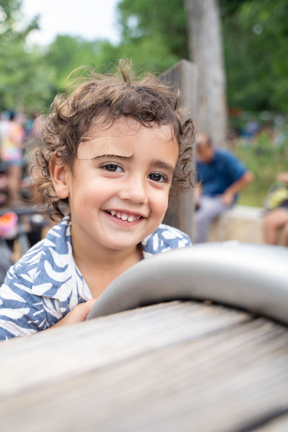 A happy child peeks over the edge of a playground structure on a sunny day.