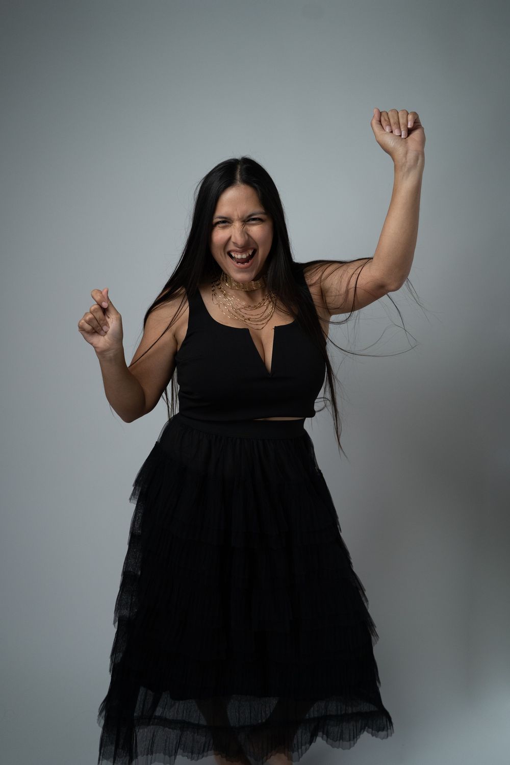 A series of joyful dance poses in a black dress against a grey studio background.