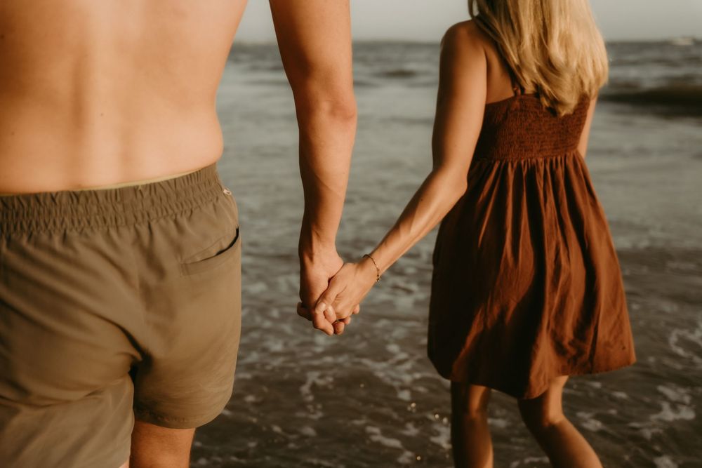 Close-up view of a couple holding hands on a dark sandy beach.