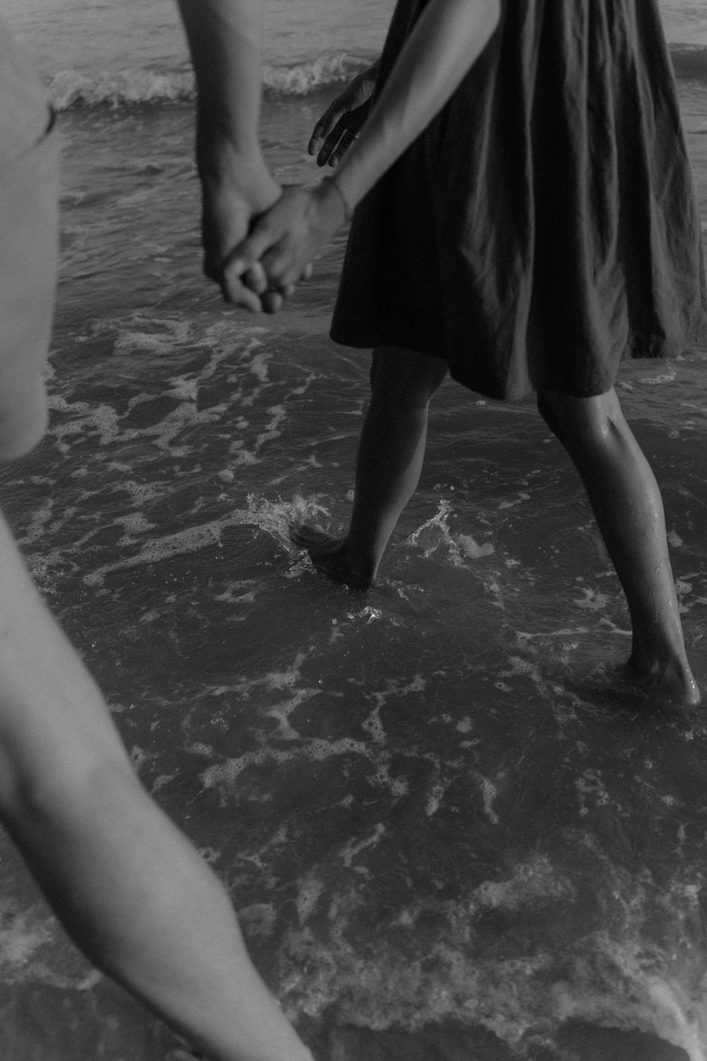 Black and white photo of legs walking in shallow ocean waves as water splashes around bare feet.
