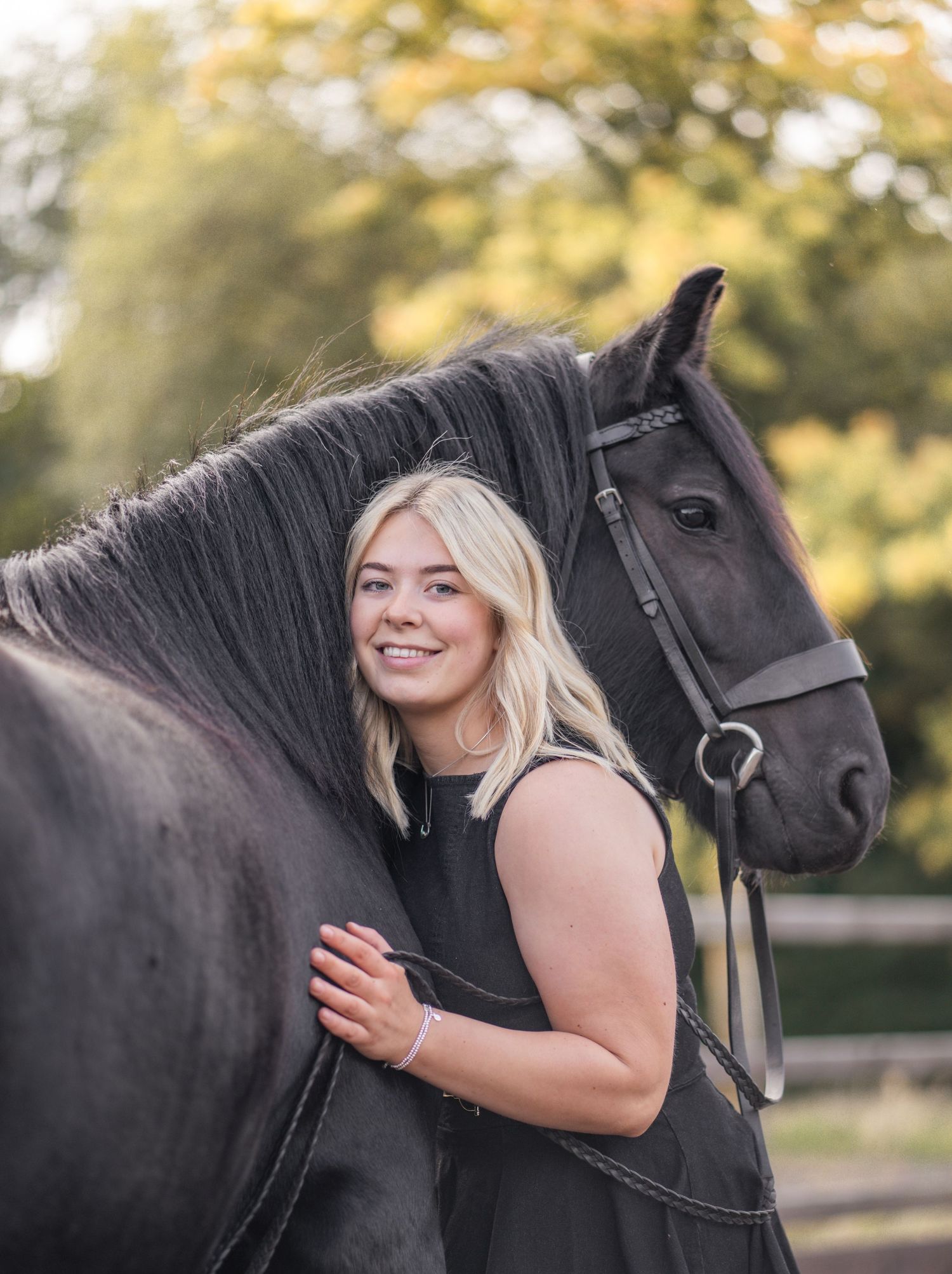 A black horse and rider share tender moments during an outdoor photo session with warm autumn lighting.