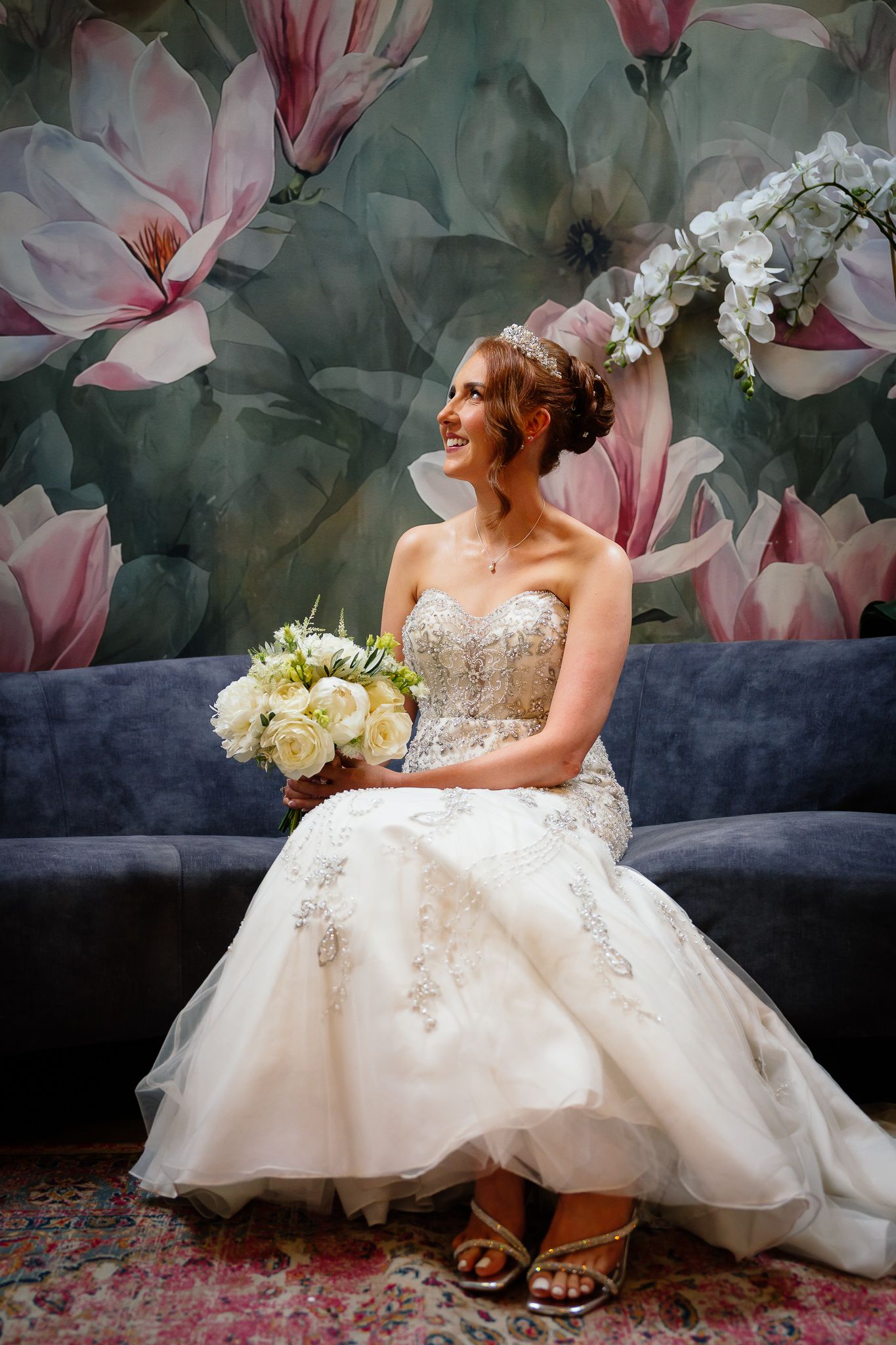 Elegant bridal portrait on vintage sofa with pink floral backdrop and white bouquet. Woodhill Hall.