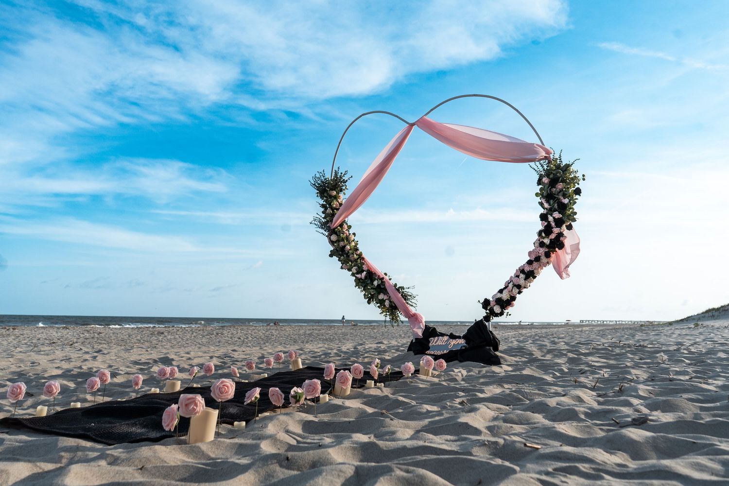 A series of beach wedding photos showing a floral arch and ceremony setup against a bright blue ocean backdrop.