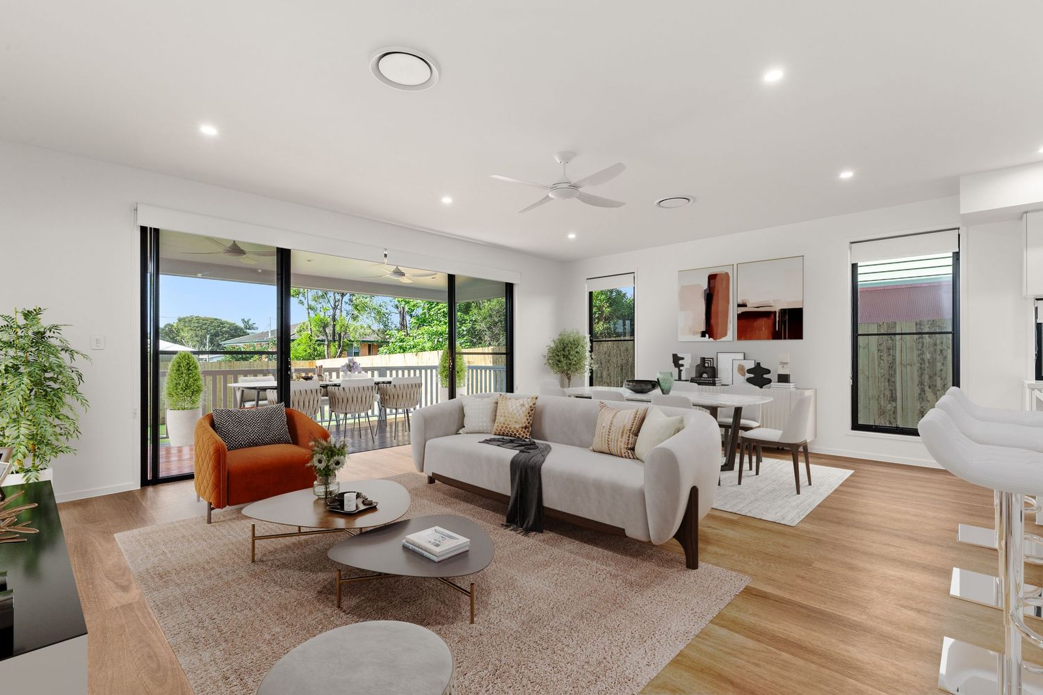 Bright open-plan living room with timber floors, ceiling fan, and large windows overlooking outdoor area.