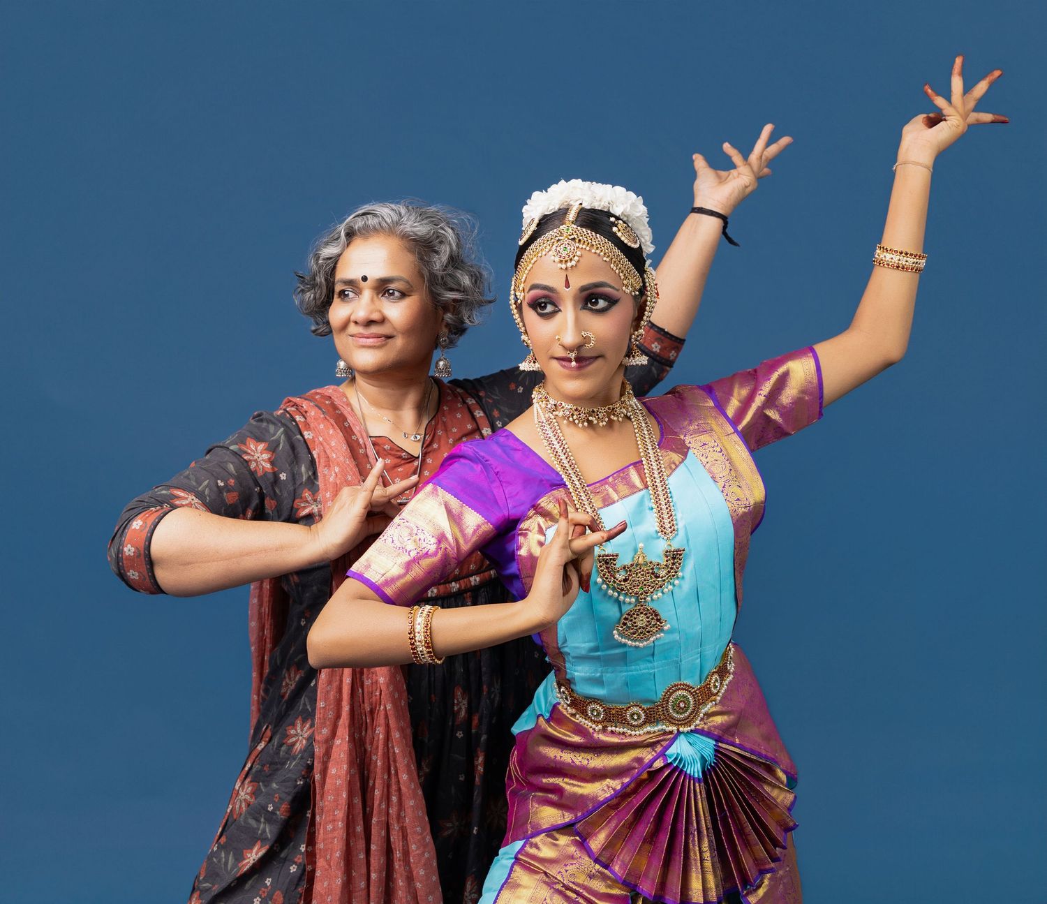 Two dancers in traditional Indian attire perform expressive dance moves against a blue backdrop in a four-part sequence.
