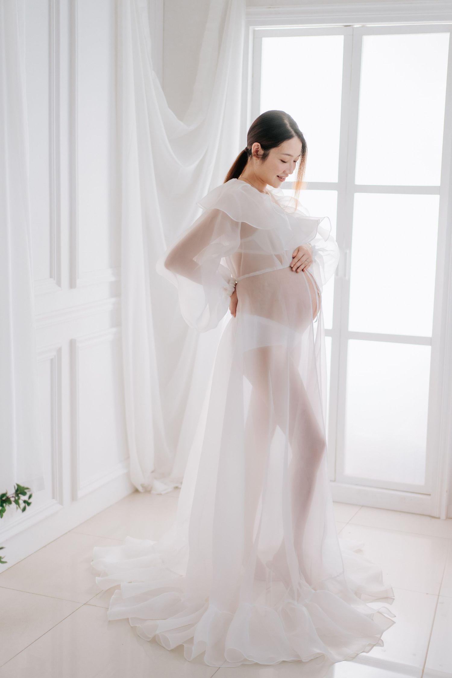 A baby in a floral dress smiles while sitting against a white backdrop with balloons.