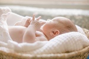 A sleeping infant lies peacefully on a white knitted blanket in soft natural lighting.