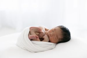 Sleeping newborn baby wrapped in white swaddle blanket on white background.