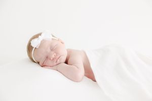 Sleeping newborn wearing white headband on white background during professional photo session.