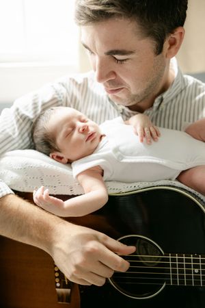 A tender moment between a parent and sleeping baby while holding an acoustic guitar.