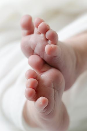 Close-up view of tiny newborn baby feet with soft pink skin against white background.